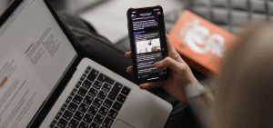 Young caucasian woman on leather couch working at a laptop while browsing her phone