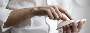 Close-up shot of a man in white shirt holding his phone and tapping on it.